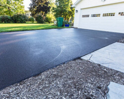 A fresh blacktop resealing job just finished on this asphalt driveway in a suburban residential district.